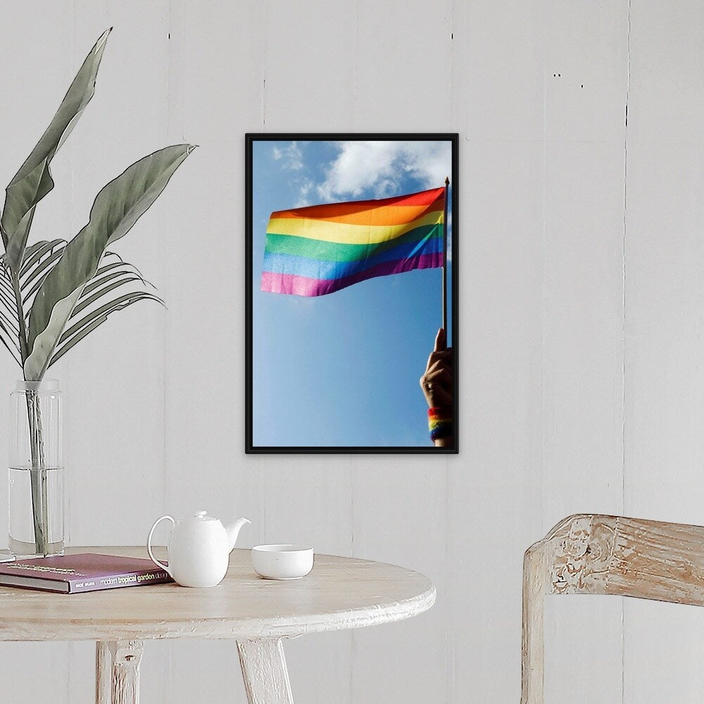"Person's hand holding rainbow-colored flag waving in the sky" Black Float Frame Canvas Art