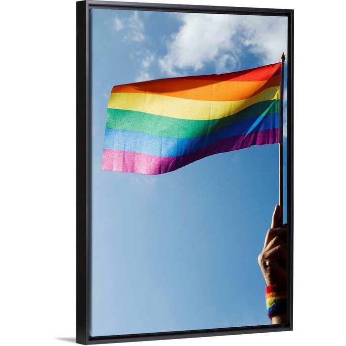 "Person's hand holding rainbow-colored flag waving in the sky" Black Float Frame Canvas Art